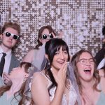 Bride and wedding party posing with props and sunglasses in front of shimmering sequin backdrop