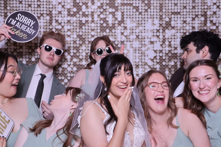 Bride and wedding party posing with props and sunglasses in front of shimmering sequin backdrop