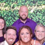 Wedding party posing in front of greenery wall with "The Cunningham's" custom backdrop