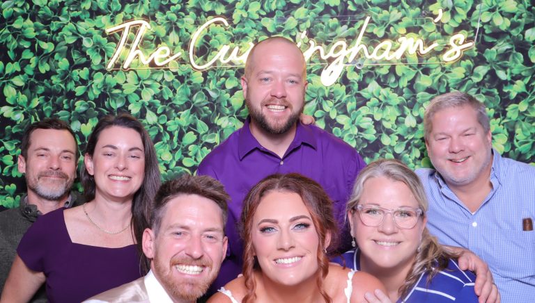 Wedding party posing in front of greenery wall with "The Cunningham's" custom backdrop