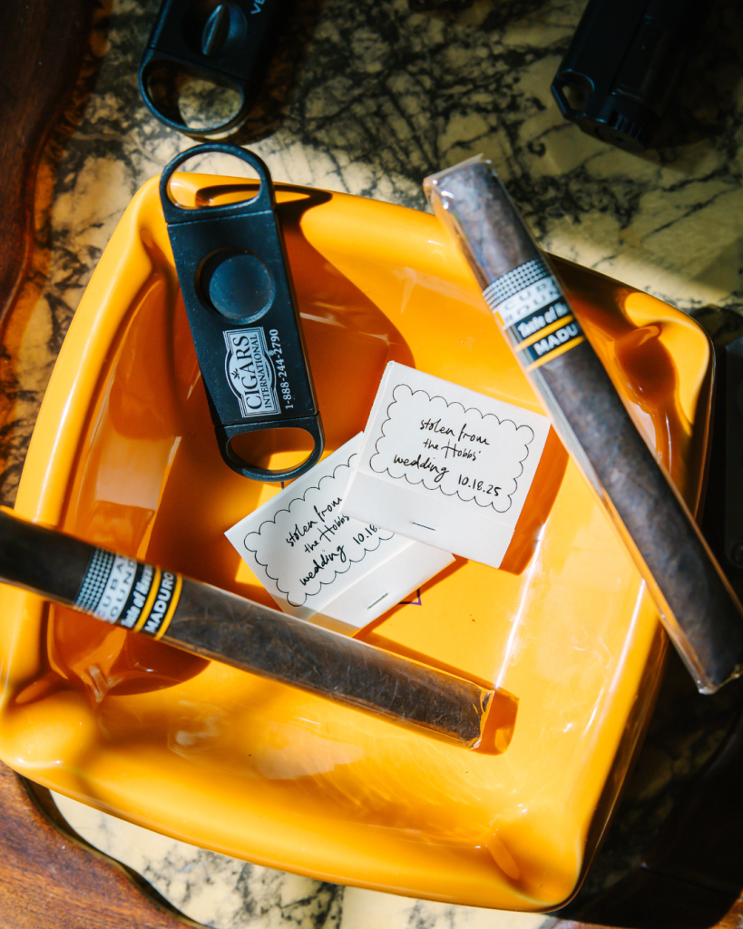 Yellow ashtray with cigars, cigar cutter, and personalized note reading "stolen from the Harris wedding, 10-18-25"