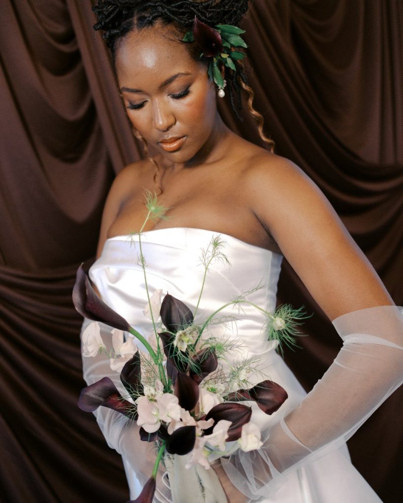 Bride in white strapless gown holding modern bouquet with dark calla lilies and delicate greenery