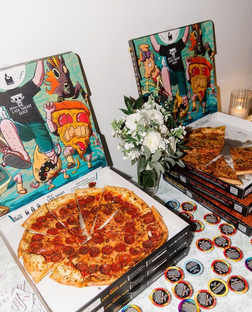 Late-night pepperoni pizzas displayed with colorful illustrated pizza boxes and white floral centerpiece for wedding reception