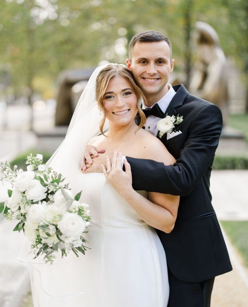 McKenzie and Michael pose together outdoors at Columbus Museum with white bouquet and museum sculptures in background