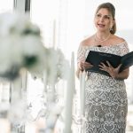Wedding officiant in white lace dress holding ceremony book with pearl necklace and elegant updo