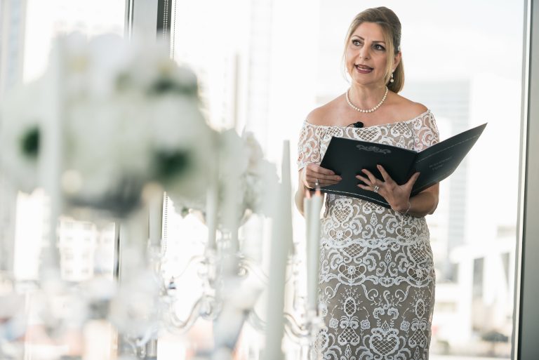 Wedding officiant in white lace dress holding ceremony book with pearl necklace and elegant updo