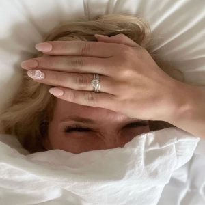 Bride covering her face with her hand showing diamond engagement ring and pink manicure