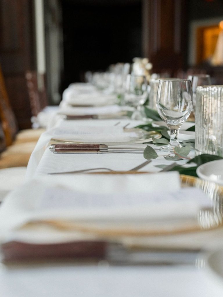 Elegant wedding reception table with white plates, crystal glasses, and eucalyptus garland runner