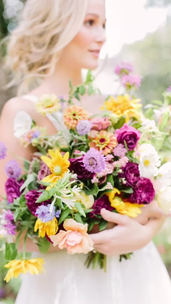 Bride holding vibrant bouquet with yellow, purple, and pink flowers in soft focus