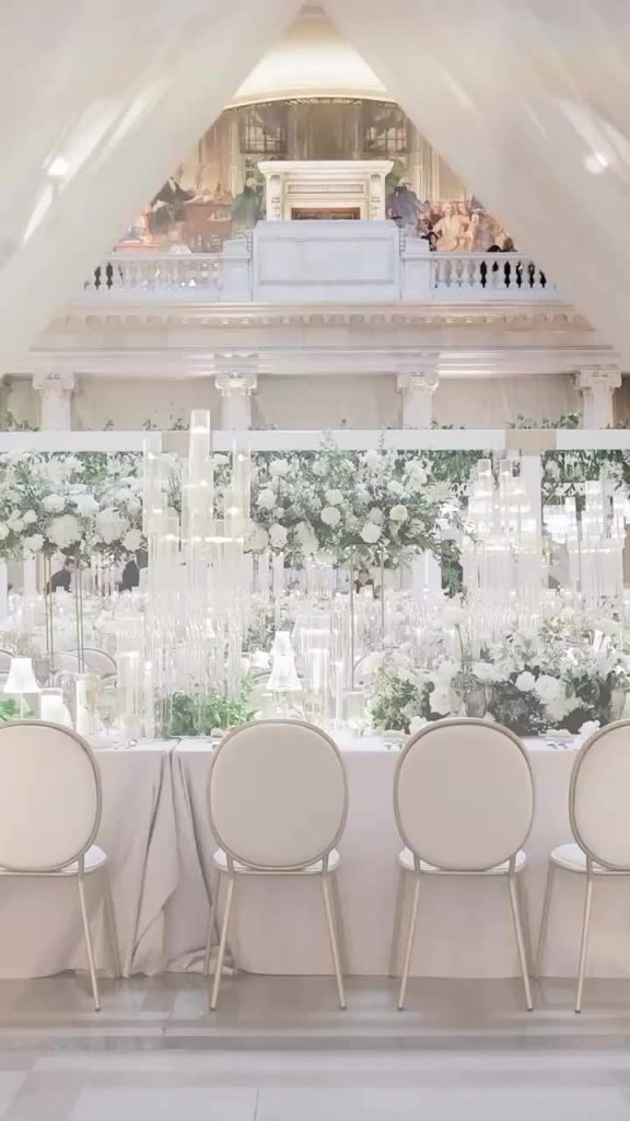 Elegant white wedding reception with tall floral centerpieces, round back chairs, and ornate balcony at Cleveland venue