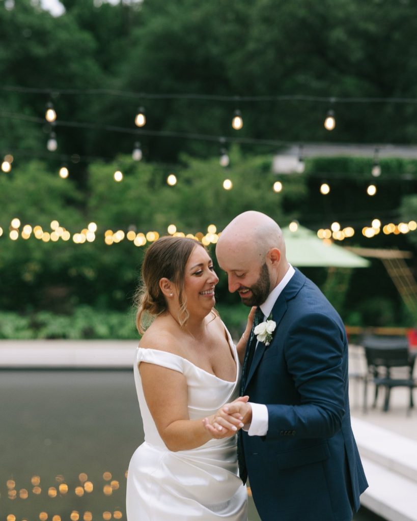 Katy and Steve share an intimate moment during their first dance under string lights at their outdoor botanical garden reception