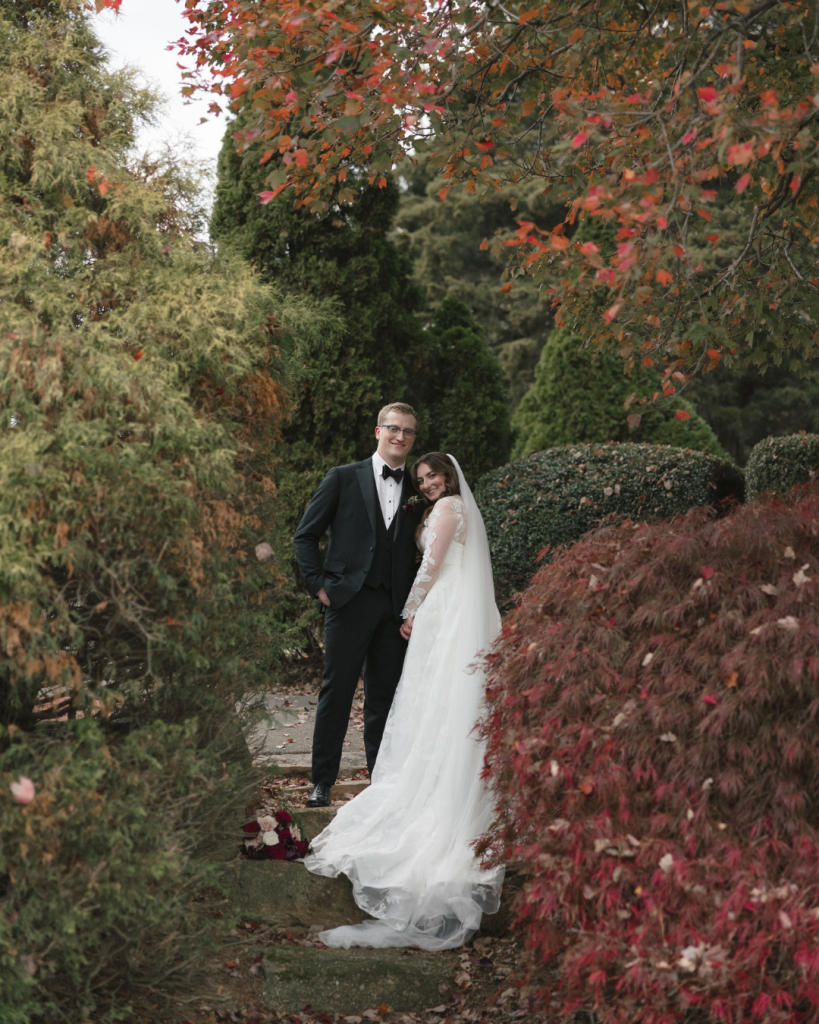 Bride and groom posing on garden path surrounded by vibrant fall foliage