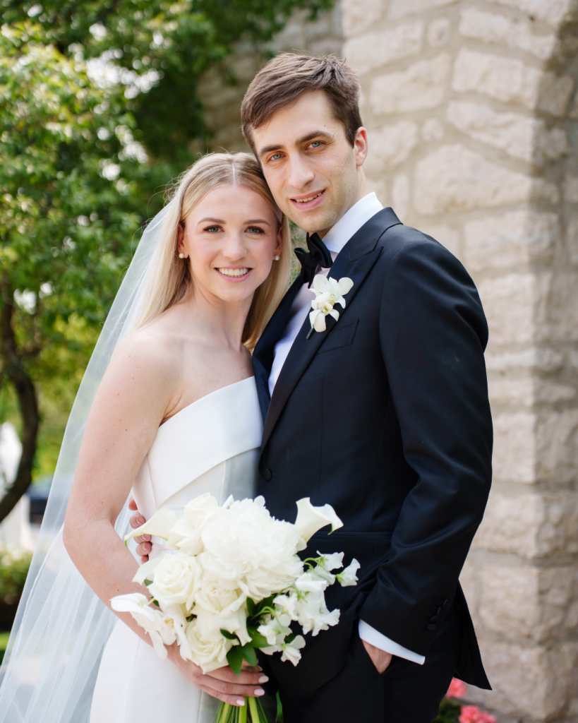 Marielle and Kyle pose outdoors, bride in strapless white gown with veil holding white bouquet, groom in black tuxedo