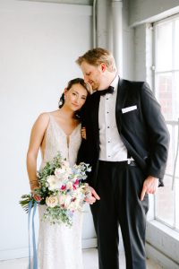 Bride and groom sharing an intimate moment by window, bride holding pink and white bouquet
