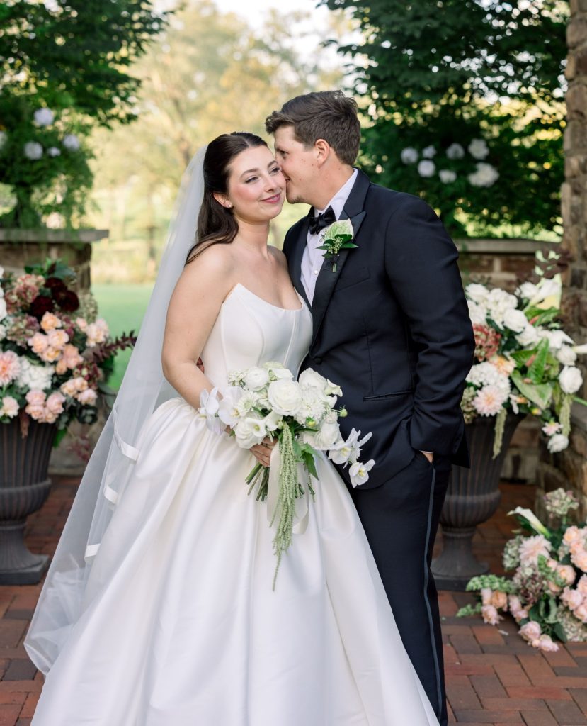 Bride and groom sharing an intimate moment in formal black-tie wedding attire with white floral arrangements