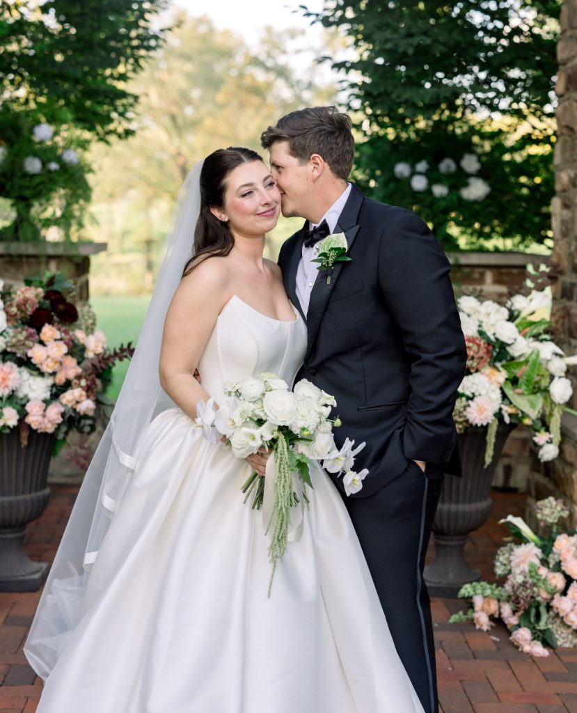 Jordan and Clayton share an intimate moment outdoors at Pinnacle Golf Club, surrounded by lush trees and colorful floral arrangements