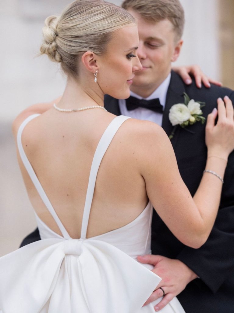 Bride and groom in intimate embrace showing bride's open-back gown with bow detail and elegant updo