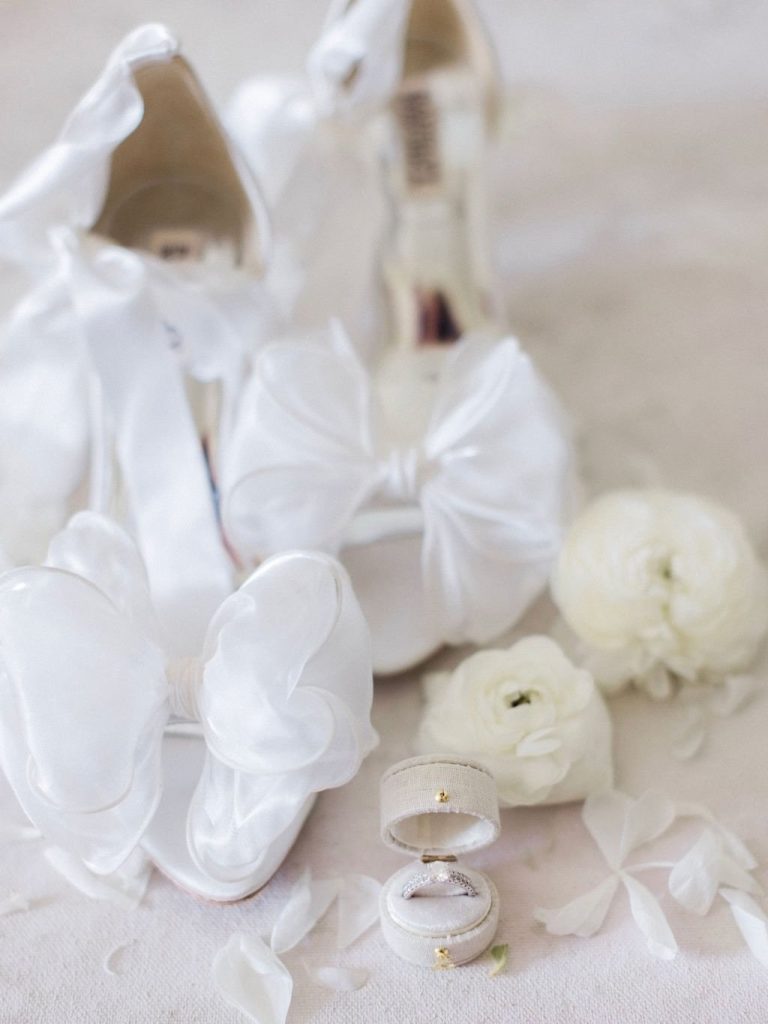 Wedding rings in velvet box displayed with white bridal shoes and white ranunculus flowers
