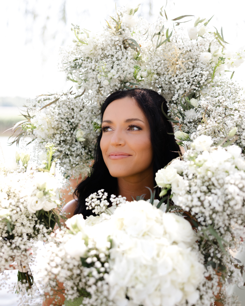 Bride Hannah surrounded by lush white baby's breath and ranunculus bouquets framing her face