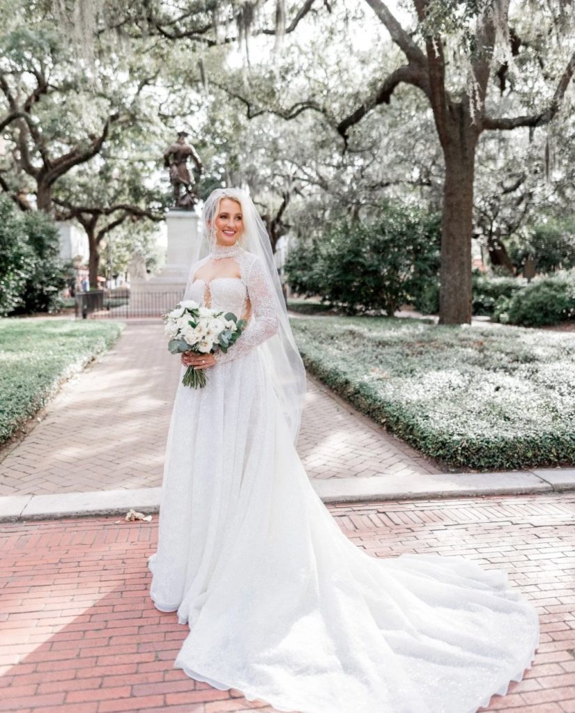 Bride Anna in lace wedding gown with cathedral veil holding white and eucalyptus bouquet in historic Savannah square