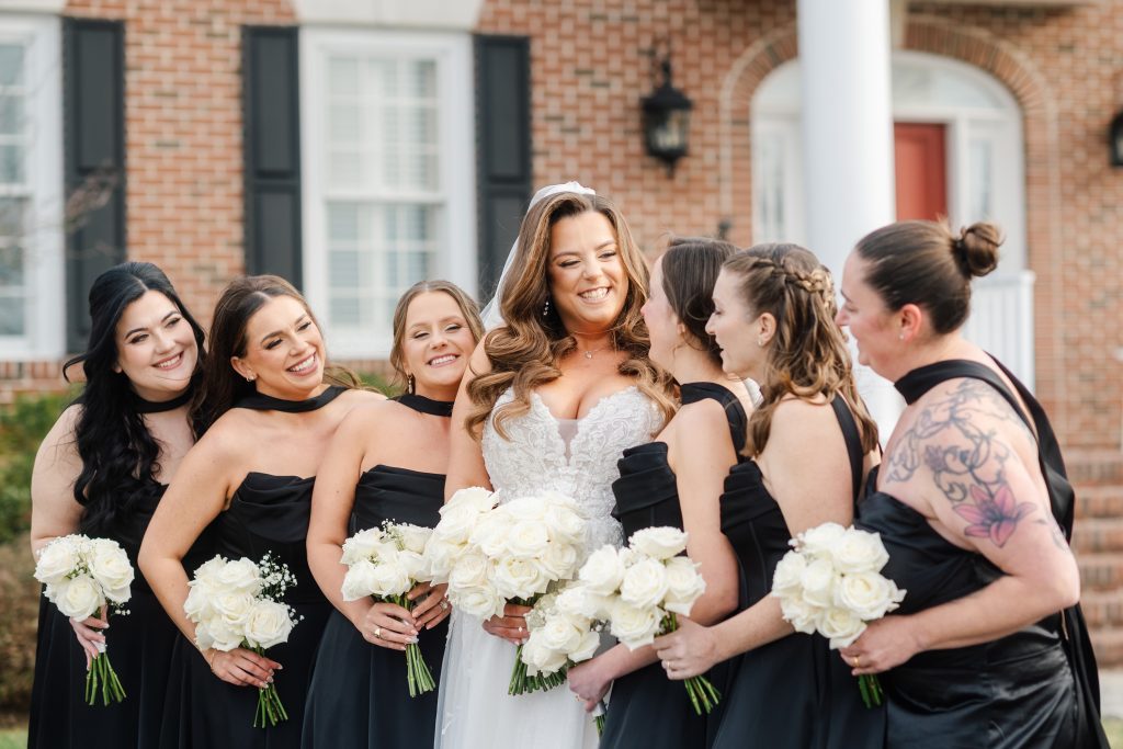 Bride with bridesmaids in black dresses holding white bouquets at King Cole Farm wedding in Dover Delaware