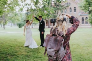 Wedding guest photographing bride and groom in background on outdoor lawn