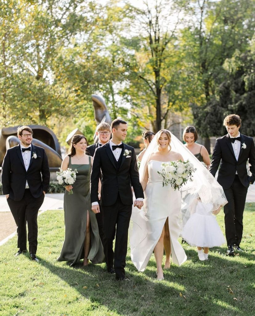 Wedding party walking outdoors at Columbus Museum with bridesmaids in olive and black gowns, groomsmen in black tuxedos