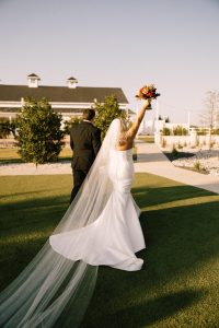 Bride in flowing white wedding dress holding bouquet outdoors on green lawn