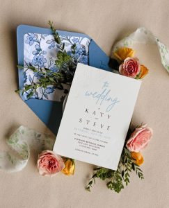 Wedding invitation suite with blue floral envelope liner, pink and yellow ranunculus blooms, and embossed invitation for Katy and Steve's Cleveland Botanical Garden wedding