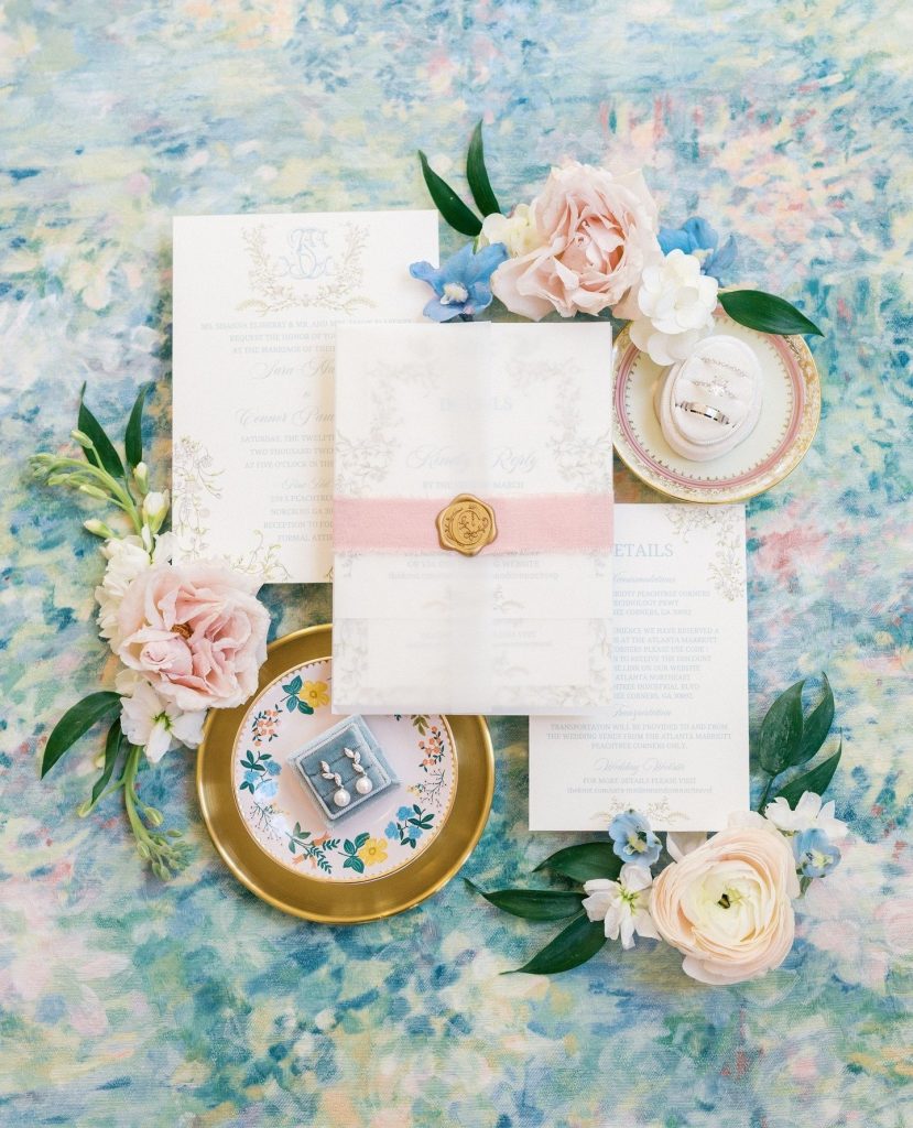 Wedding invitation suite with blush and blue watercolor details, gold wax seal, and fresh flowers on vintage china plates