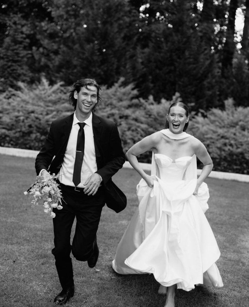 Joyful newlyweds running hand-in-hand across manicured lawn in black and white outdoor wedding portrait