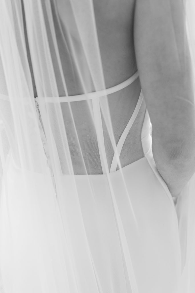 Close-up detail of wedding dress back featuring sheer paneling with geometric white straps and zipper