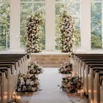Romantic chapel ceremony setup with tall floral columns, rose-lined aisle, and candlelight