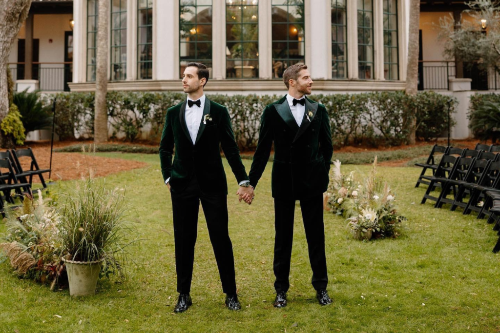 Two grooms in black tuxedos holding hands at outdoor wedding ceremony in Canton