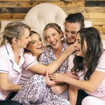 Bridesmaids in floral dresses laughing together and looking at a phone
