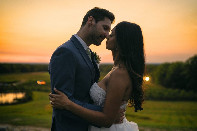 Bride and groom embrace at sunset overlooking golf course with golden sky