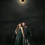 Couple holding hands beneath dramatic total solar eclipse in evening field