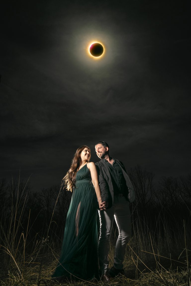 Couple holding hands beneath dramatic total solar eclipse in evening field