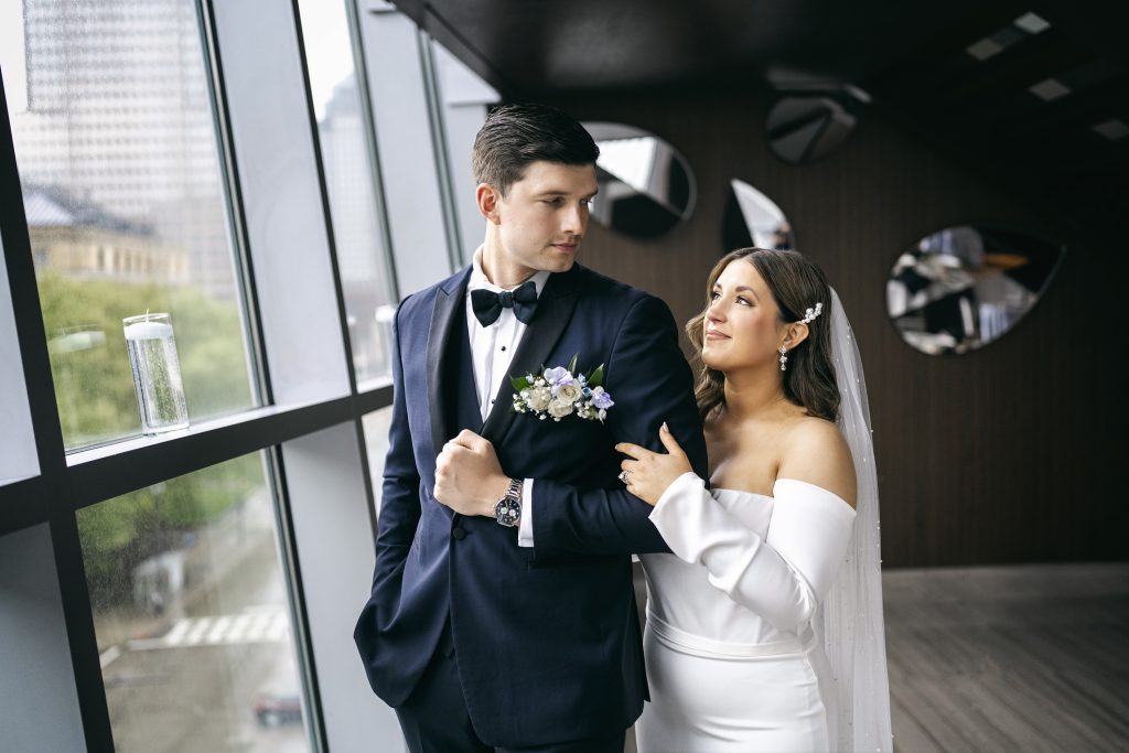 Bride and groom walking hand in hand by modern windows in formal wedding attire