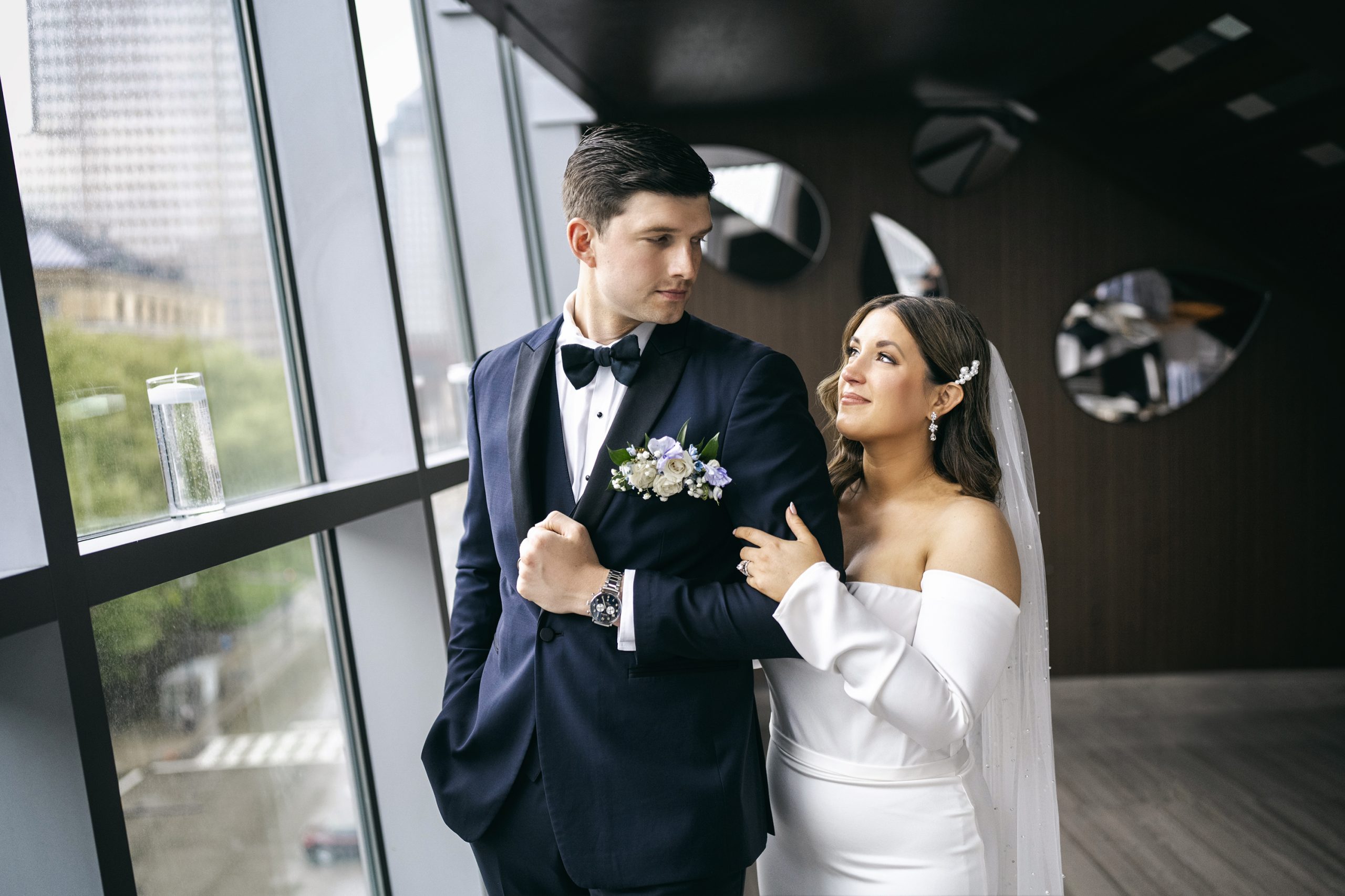 Bride and groom walking hand in hand by modern windows in formal wedding attire