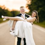 Groom carrying bride on a country road at sunset