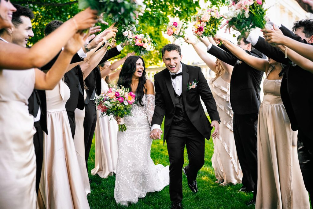 Newlyweds walking under raised bouquets held by wedding party in outdoor ceremony