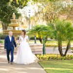 Newlyweds walking hand-in-hand through park with fountain and greenery