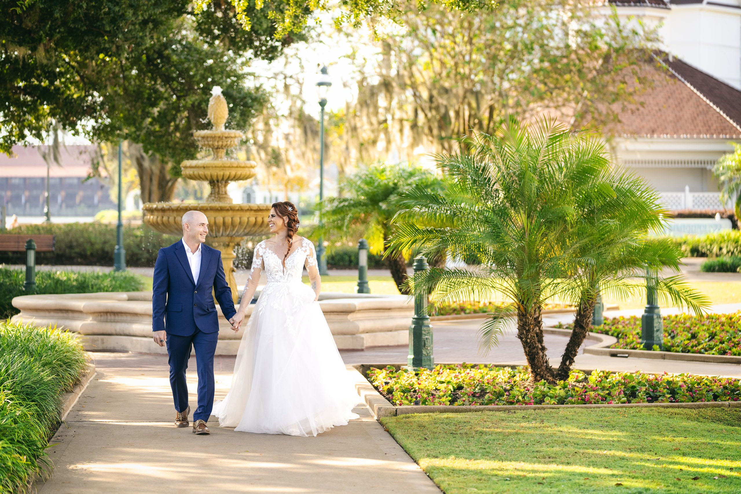 Newlyweds walking hand-in-hand through park with fountain and greenery