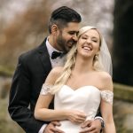Bride and groom laughing together outdoors, bride in off-shoulder lace wedding gown with veil