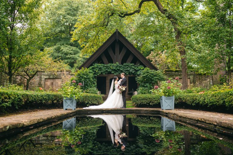 Bride and groom embracing under black pavilion beside reflecting pool