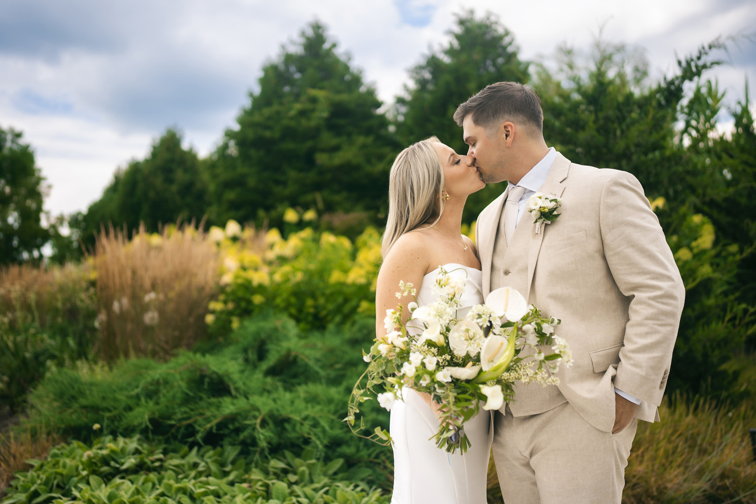 Couple sharing intimate moment in garden setting with white floral bouquet