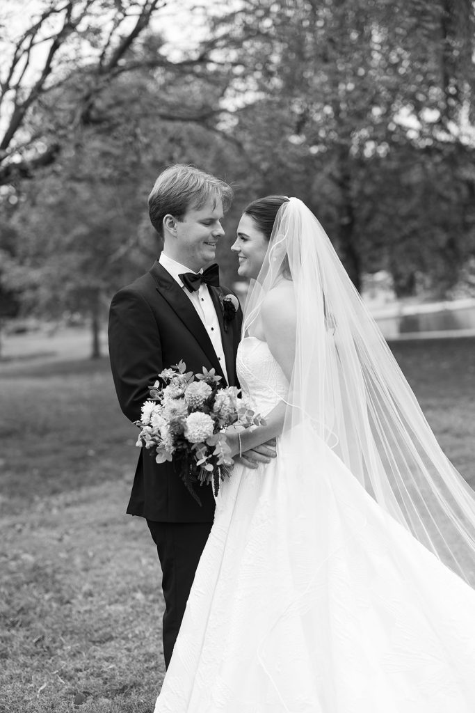 Caroline and Josh embracing in park setting, bride holding colorful bouquet with flowing cathedral veil