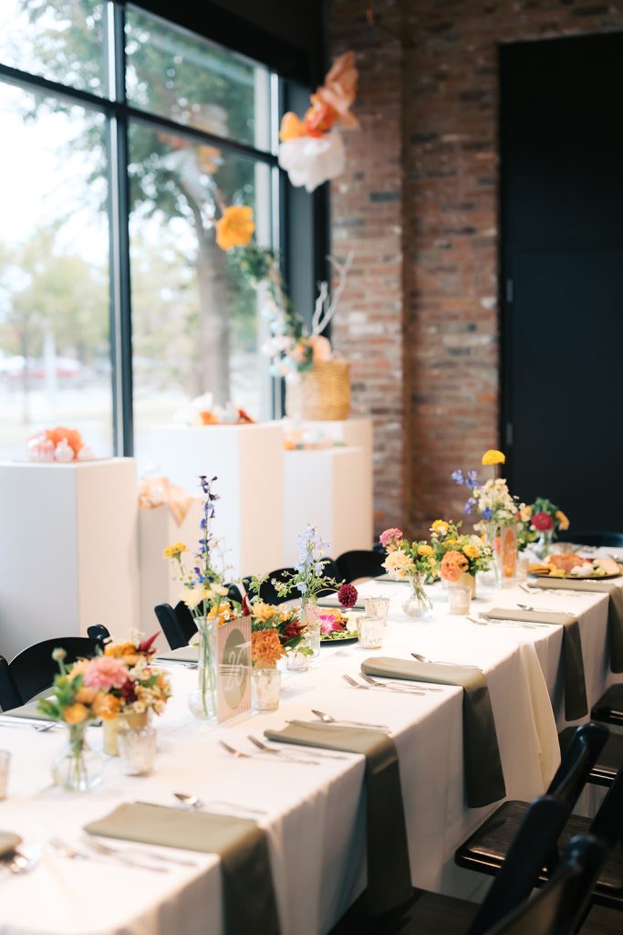Modern industrial reception venue with colorful wildflower centerpieces on white-linens tables and exposed brick walls