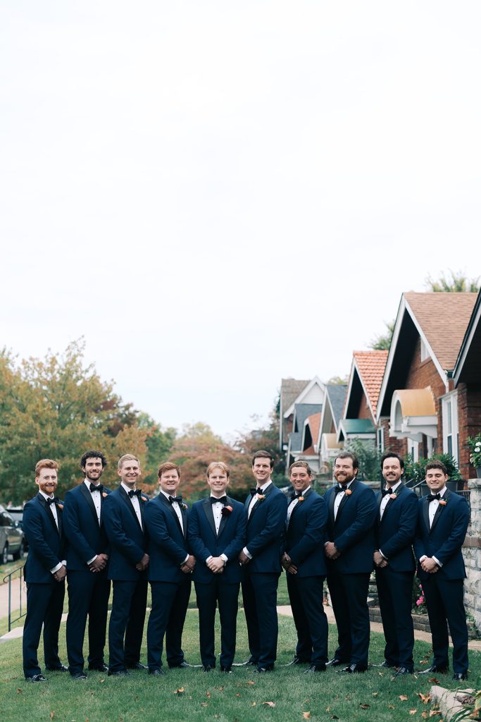 Josh and groomsmen in navy tuxedos with bow ties lined up outdoors in residential neighborhood